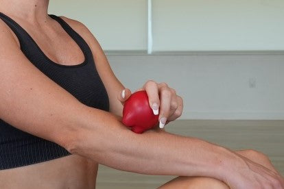 Woman using a red massage ball to apply pressure on her forearm for muscle relief. Self-massage technique helps reduce tension, improve circulation, and alleviate soreness.