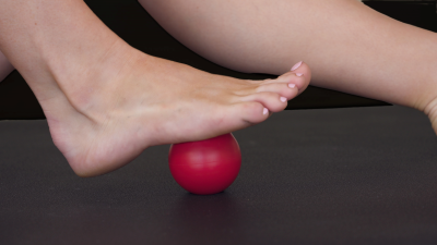 Close-up of a foot applying pressure on a red massage ball for self-massage and muscle relief. The technique helps release tension, improve circulation, and reduce foot pain.